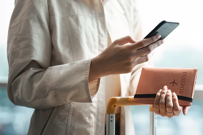 Tourist woman using mobile smartphone and holding passport with suitcase traveling between waits for flight in Airport Terminal, flight check in, Tourist journey trip concept